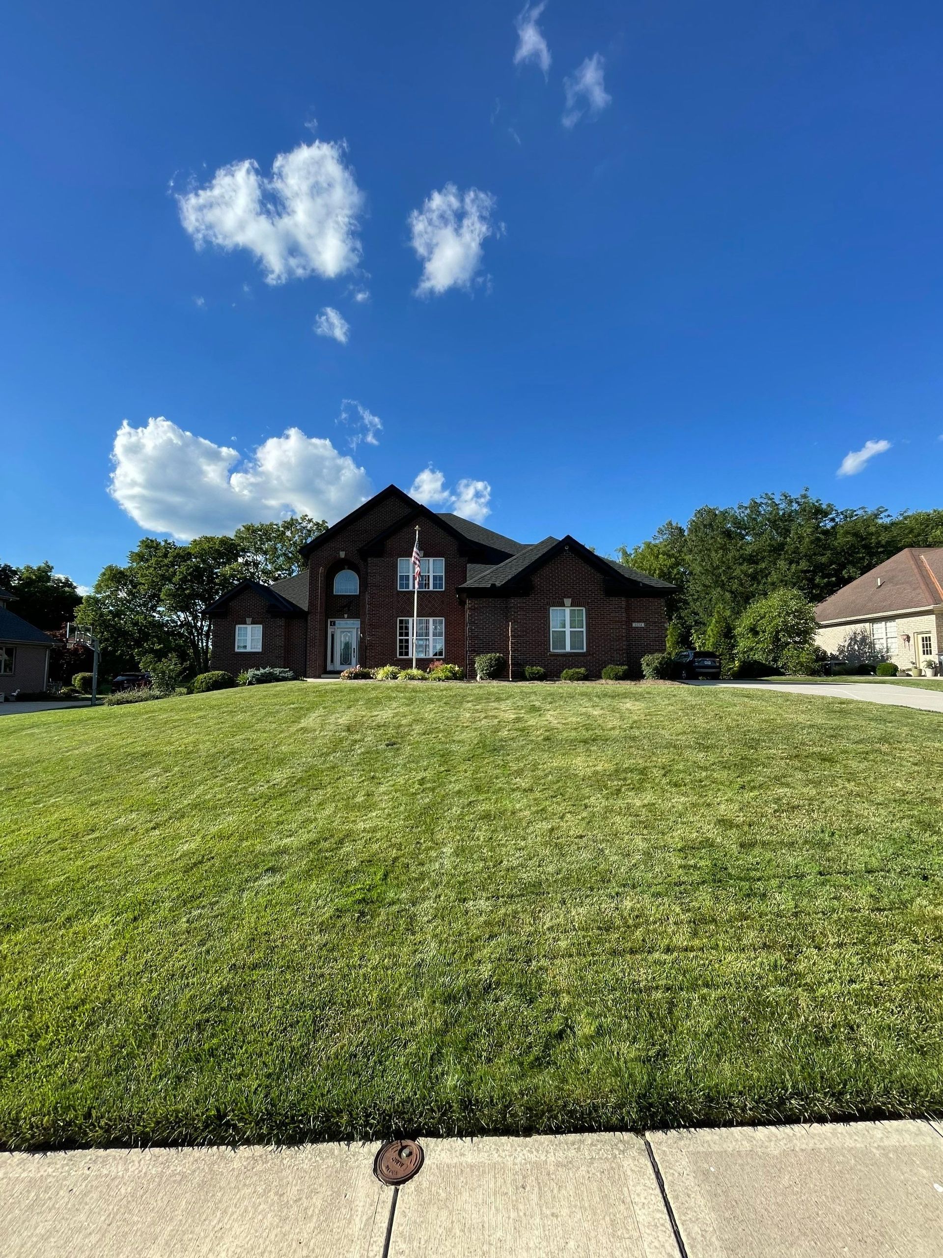 Brick house with dark roof behind a large green lawn under a bright blue sky.