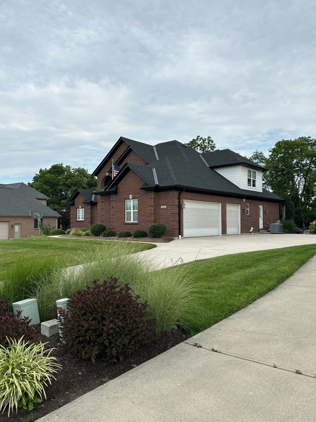 Suburban brick house with two white garage doors, sloped black roof, and a front lawn under cloudy skies
