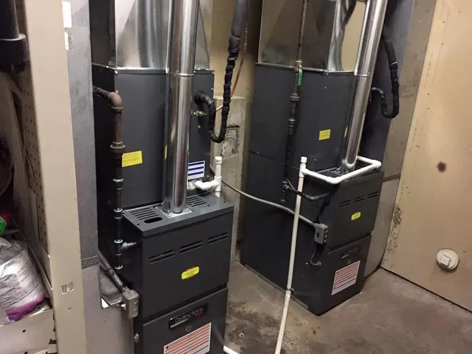 Two black HVAC furnaces with metal ducts in a narrow utility closet