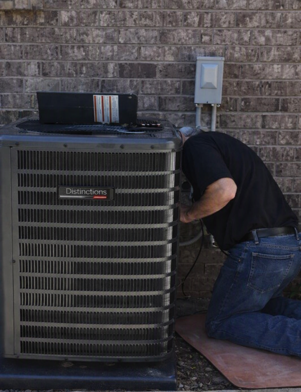 Technician kneels beside a large outdoor HVAC unit, working on the side panel.