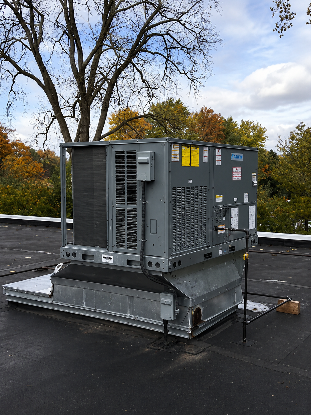 Gray HVAC unit on a rooftop platform under cloudy sky, with trees in the background