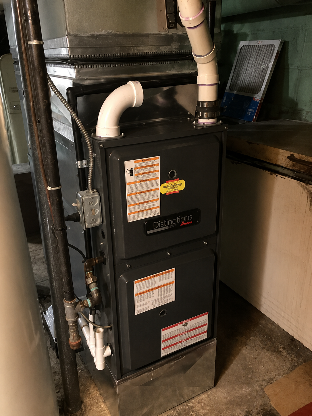 Gas furnace unit in a basement utility room with attached ducts and pipes.