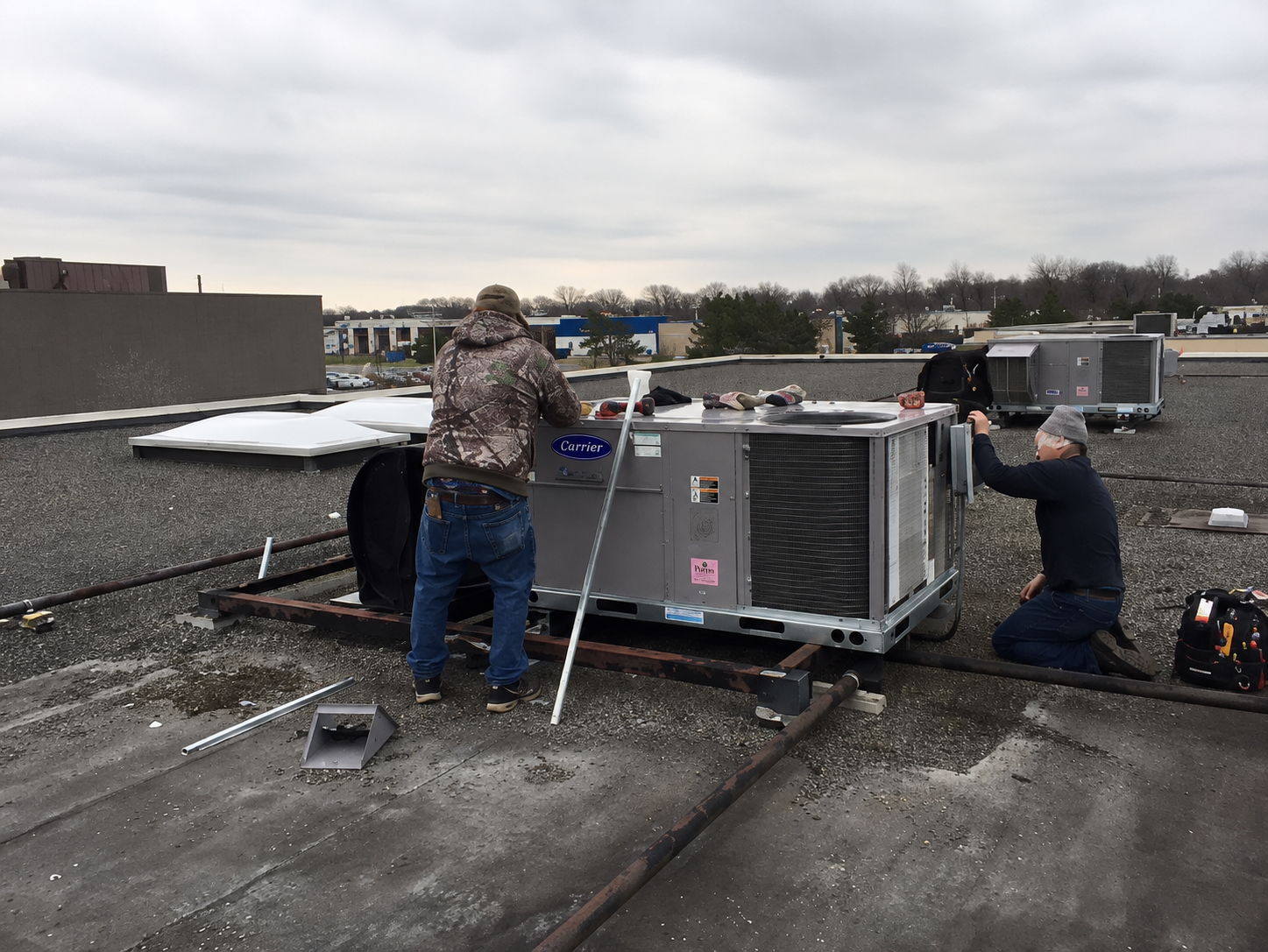 Workers installing rooftop HVAC units on a flat roof under an overcast sky