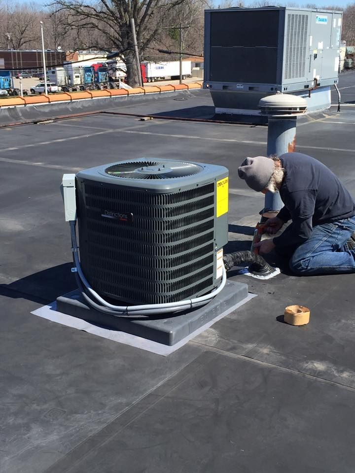 Worker kneeling beside a rooftop HVAC unit, using a tool for maintenance.