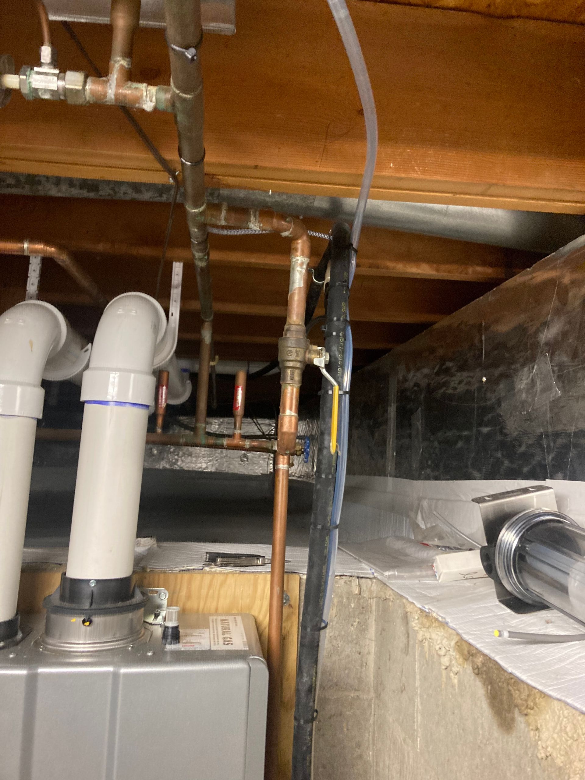 Basement ceiling with pipes, ducts, and a furnace or HVAC unit above insulation.