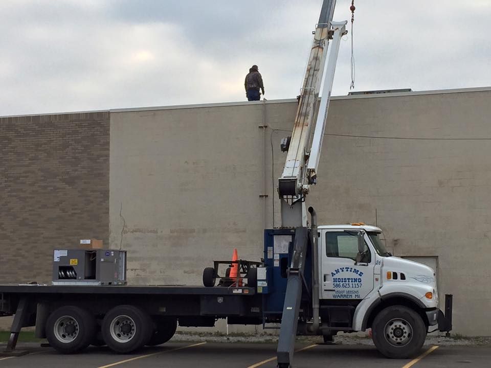 Bucket truck worker painting a large beige wall beside a brick building