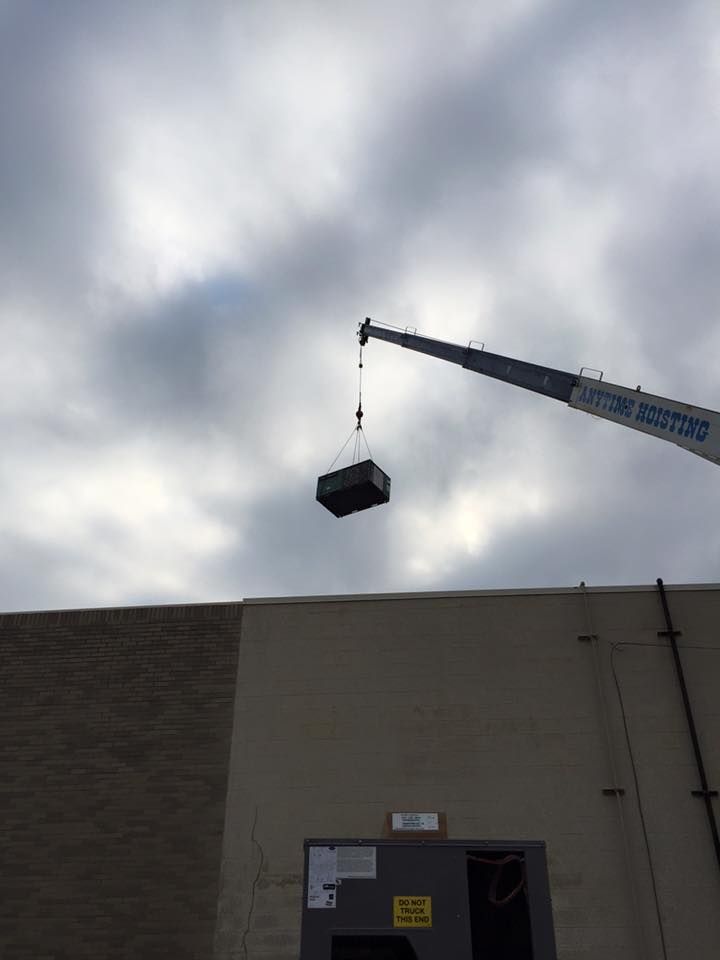 Crane lifting a black dumpster over a beige building against a cloudy sky