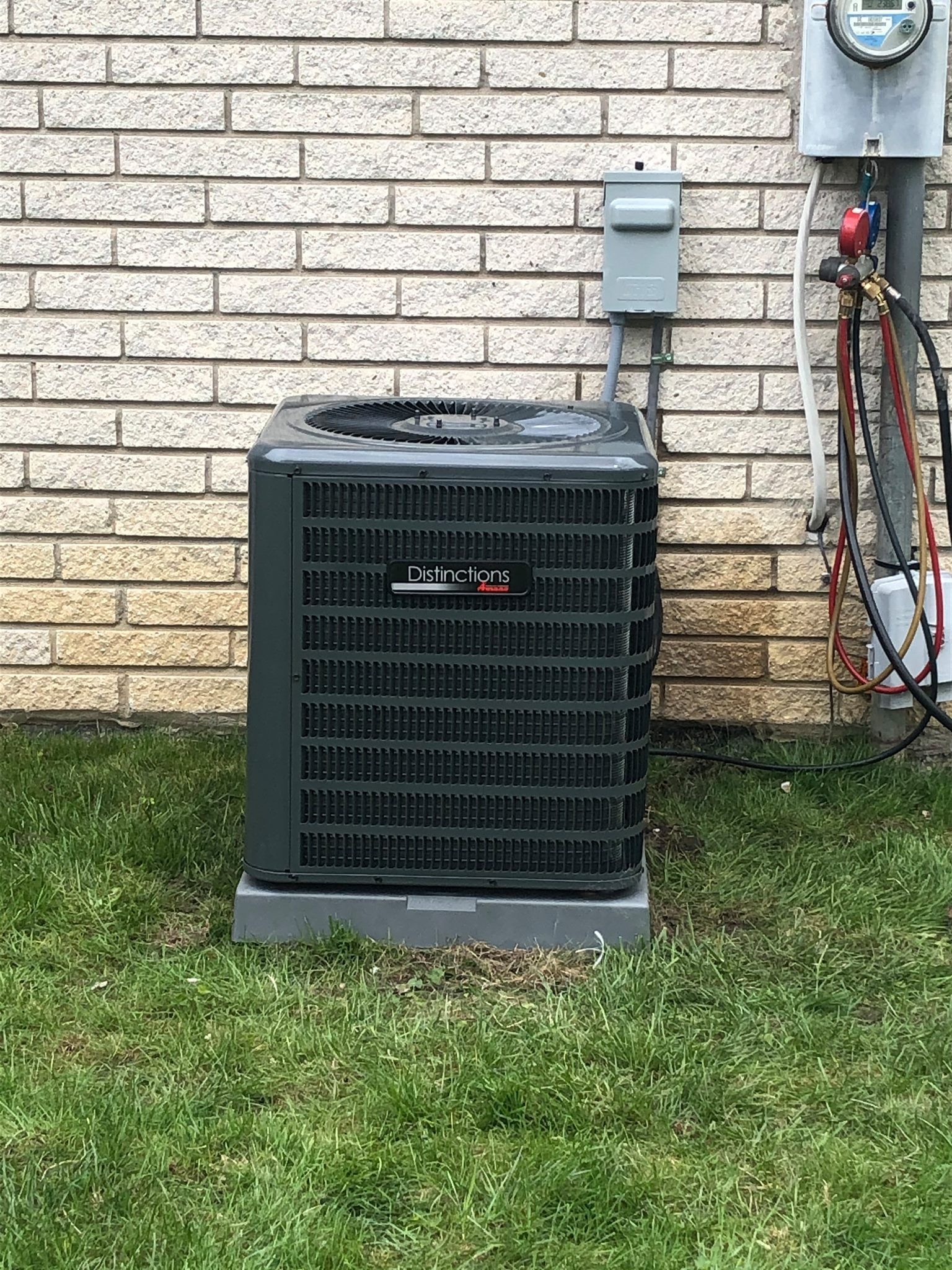 Outdoor air conditioner unit beside a brick house wall on a grassy lawn