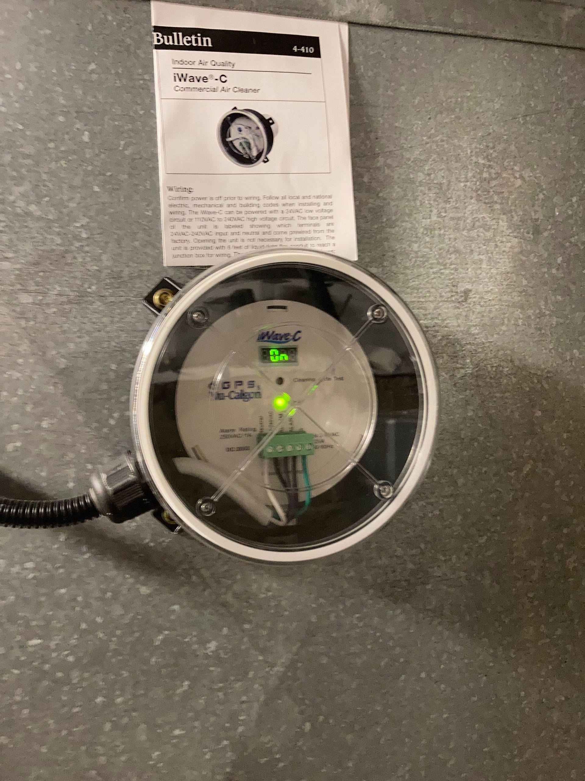 Small round device with green lights on a gray floor, next to a product instruction sheet.