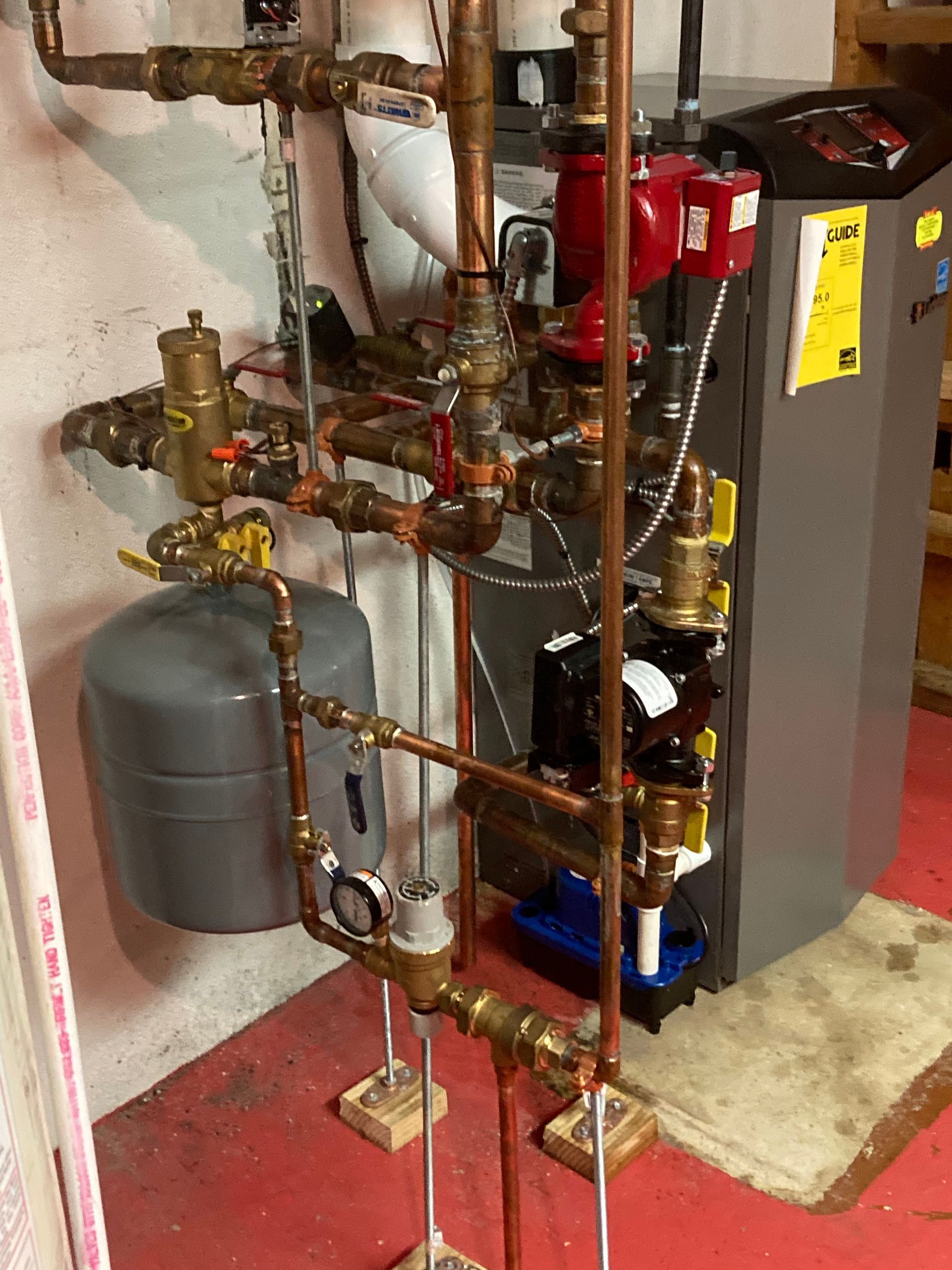 Boiler room with copper pipes, valves, red expansion tanks, and a gray furnace unit