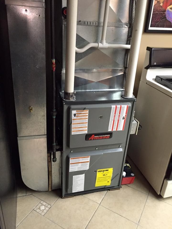 Residential furnace and ductwork in a utility closet, with exposed pipes and tiled floor.
