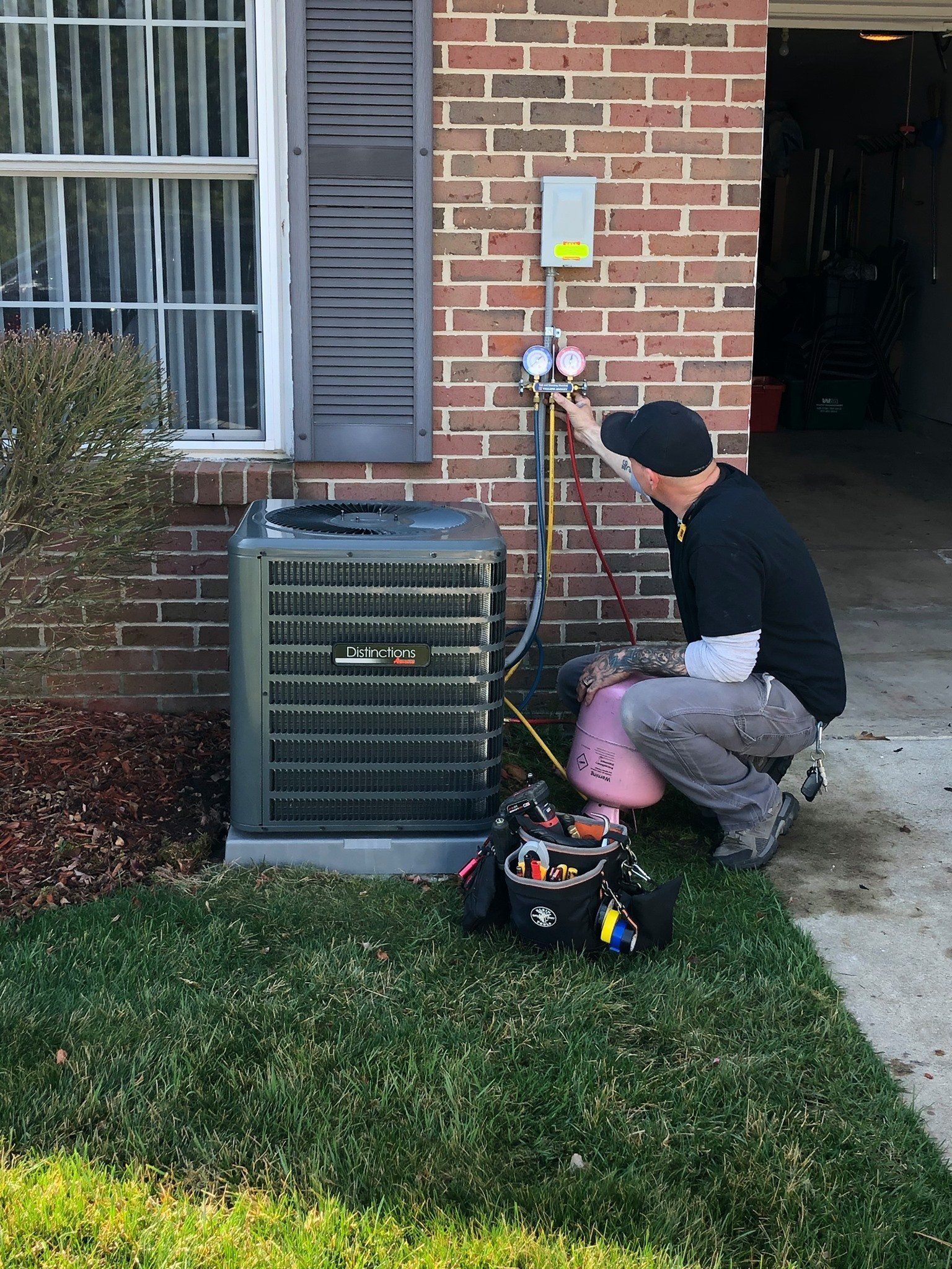 Technician inspecting an outdoor air conditioning unit beside a brick house