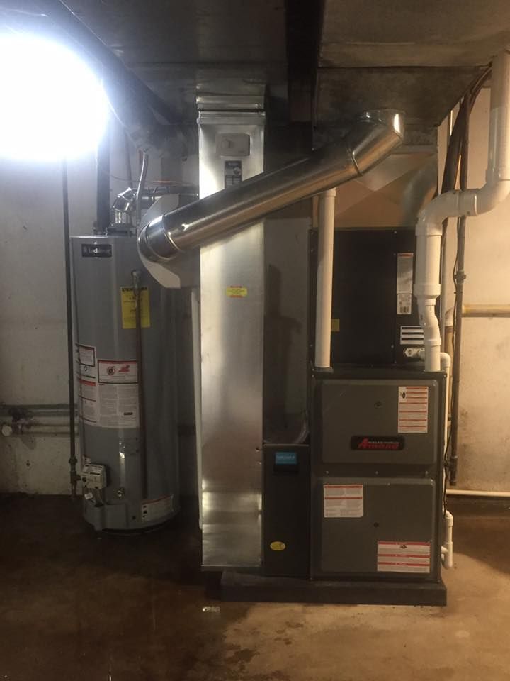 Basement utility room with a furnace, water heater, and exposed pipes under bright light