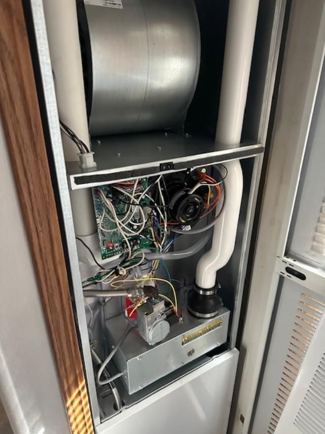 Open HVAC/air handler cabinet with wiring, ducts, and metal components inside a closet.