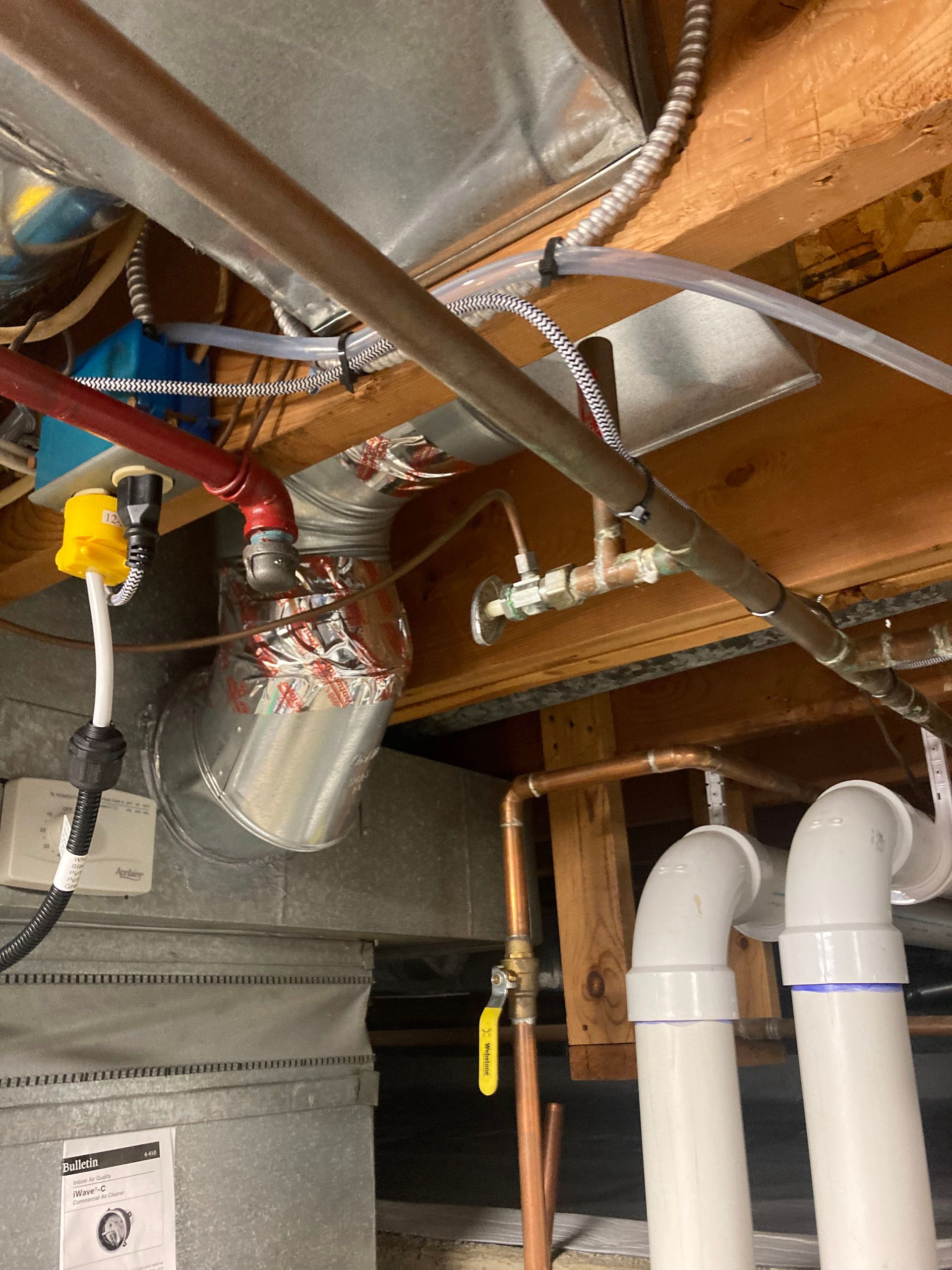 Under-sink plumbing with white PVC pipes, insulated ducts, and exposed joists in a basement ceiling