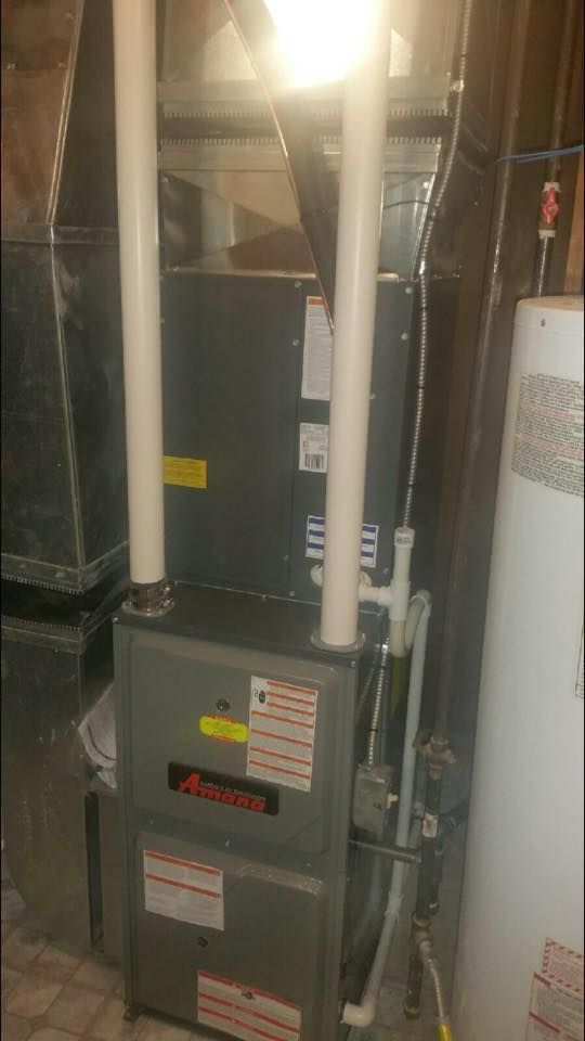 Indoor HVAC furnace and ductwork in a utility closet with pipes and a water heater.