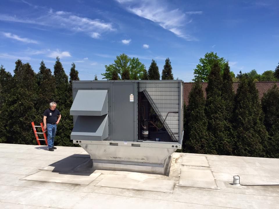 Large rooftop HVAC unit beside a worker on a flat roof under a clear blue sky.