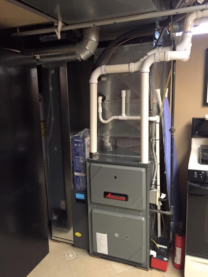 Basement furnace and HVAC unit with white ductwork and black appliances in a utility room