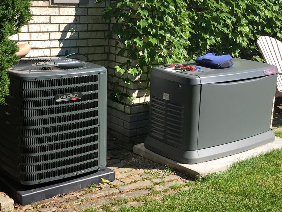 Two outdoor HVAC units beside a brick house on a patio and grass.