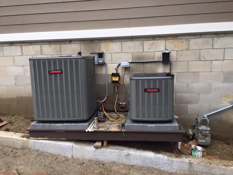 Two outdoor air conditioning units on a concrete pad beside a cinderblock wall.