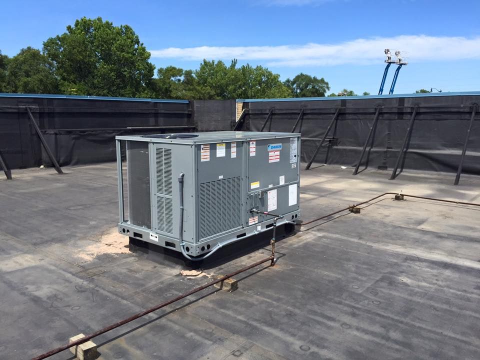 Large gray HVAC unit on a rooftop, surrounded by black safety netting and trees in the background