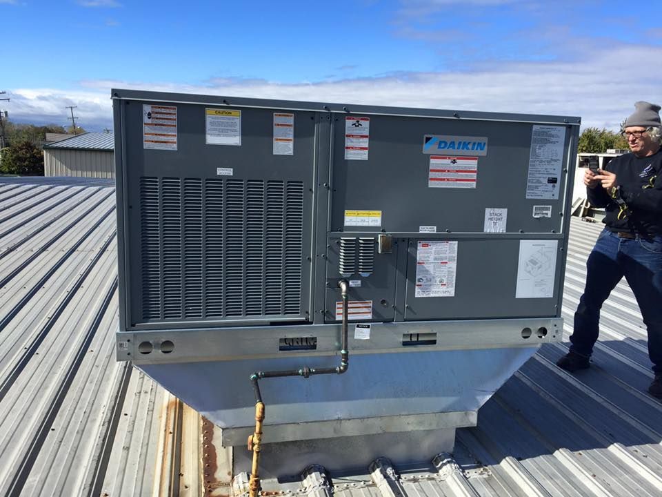 Rooftop HVAC unit with ducting and a worker standing nearby on a metal roof.