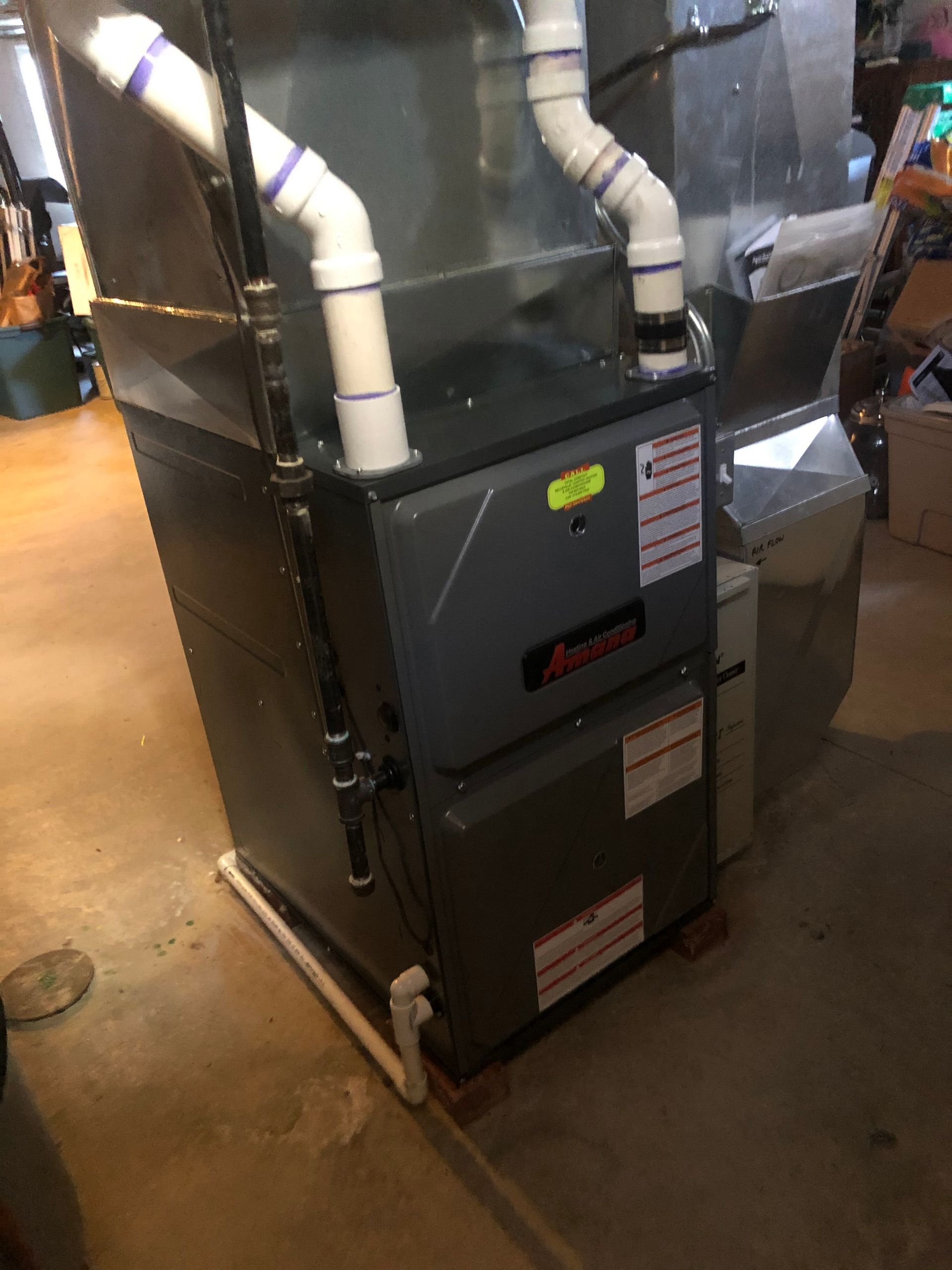 Basement furnace with white PVC pipes and ductwork beside a concrete floor