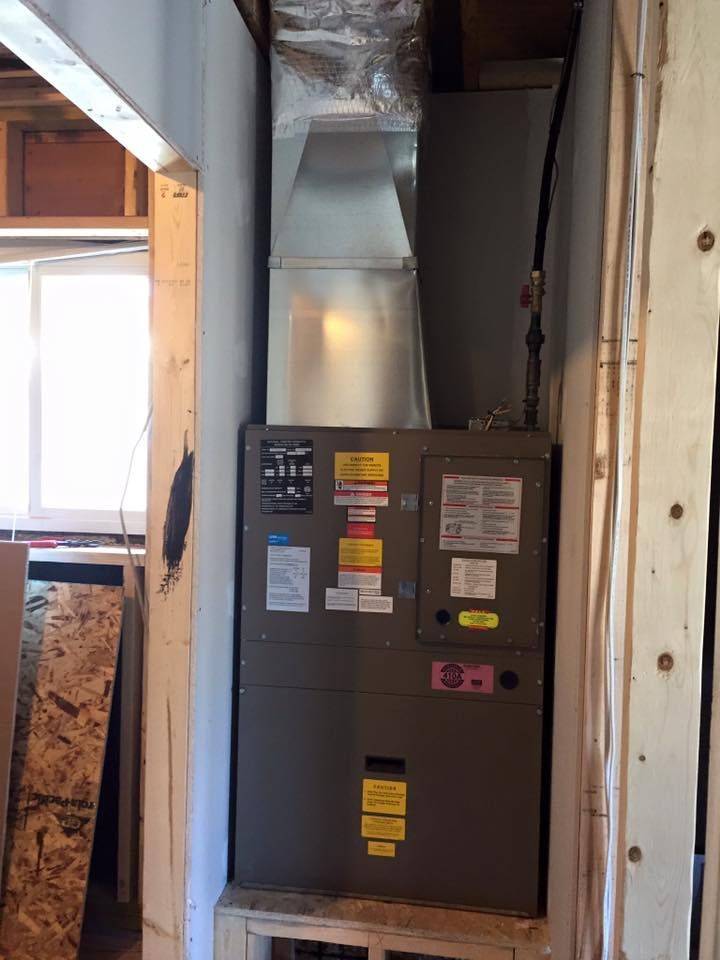Gray furnace in a utility room with exposed wooden framing and ductwork.