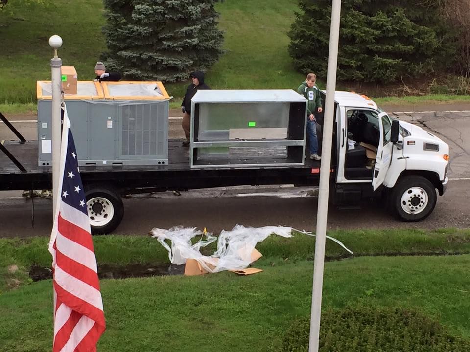 White utility truck with equipment parked on a street beside an American flag in a grassy yard.