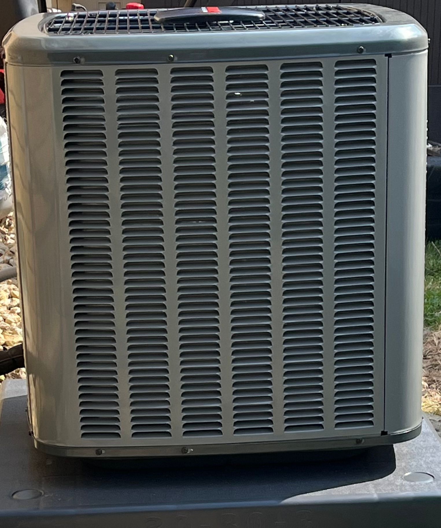 Outdoor air conditioning unit with gray metal grille and fan on top