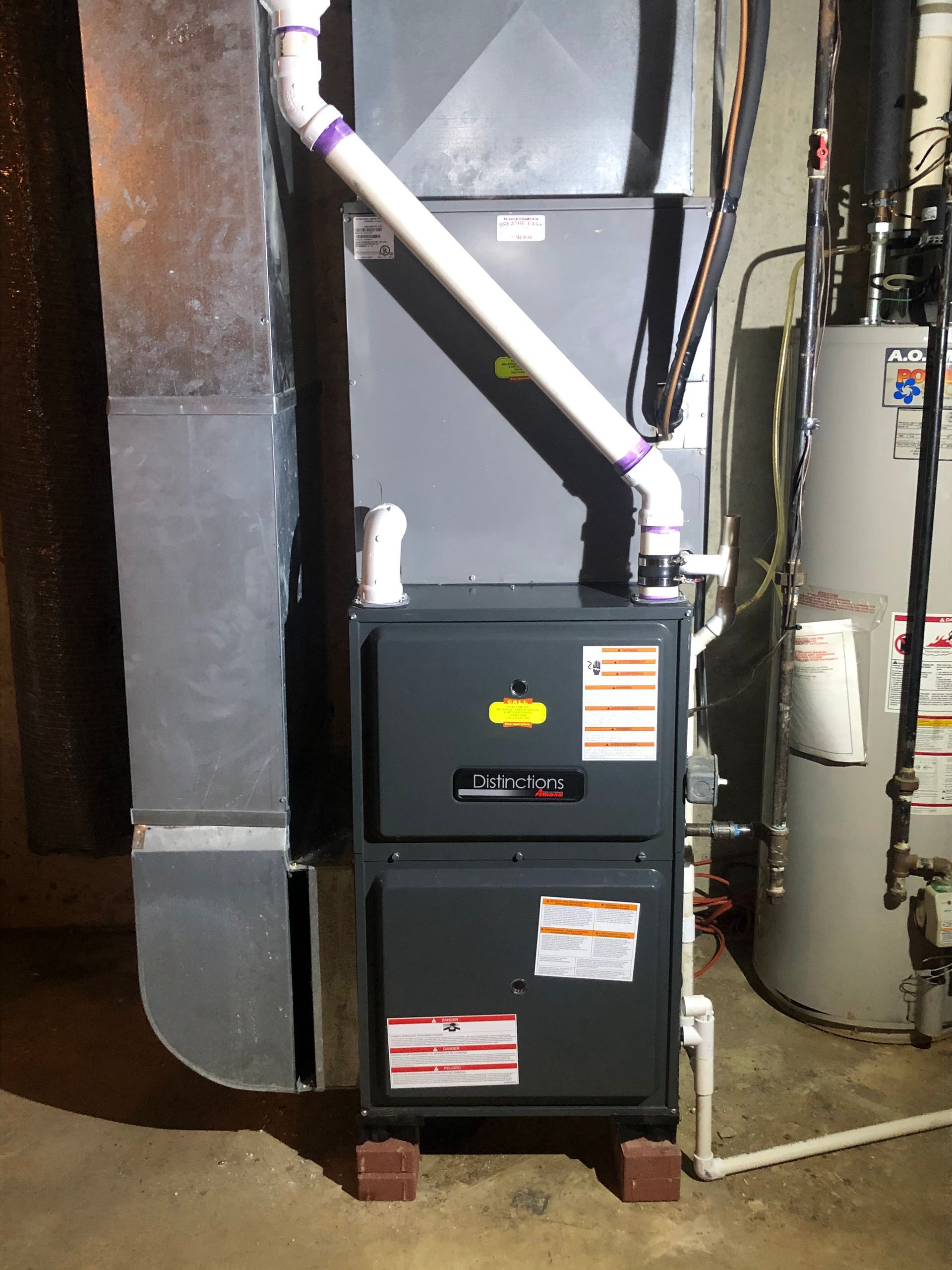 Black furnace and silver ductwork in a utility room with exposed pipes and equipment