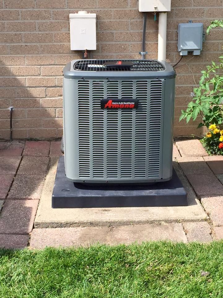 Outdoor central air conditioner unit beside a brick house on a concrete pad and lawn