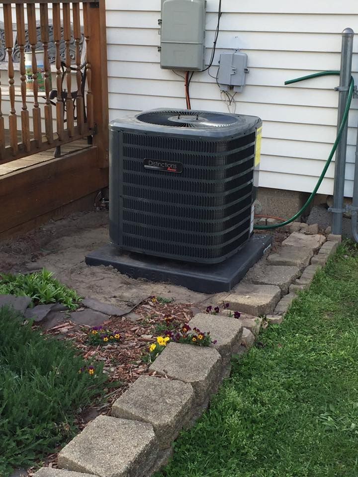 Outdoor air conditioner unit beside a house, next to a wooden deck and garden edging.