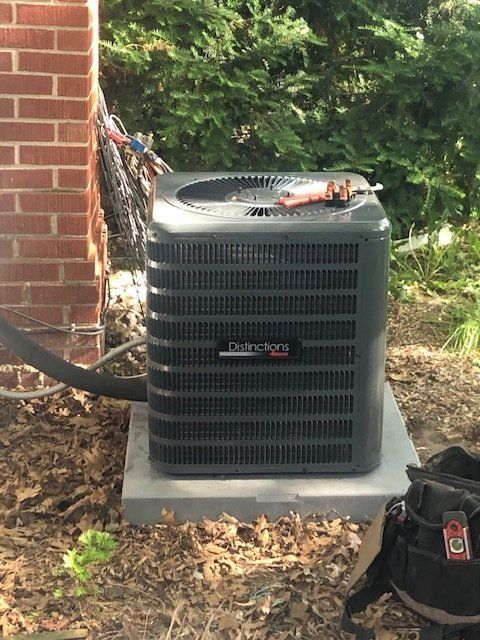 Outdoor HVAC unit beside a brick wall, with tools on top and a black tool bag in front.
