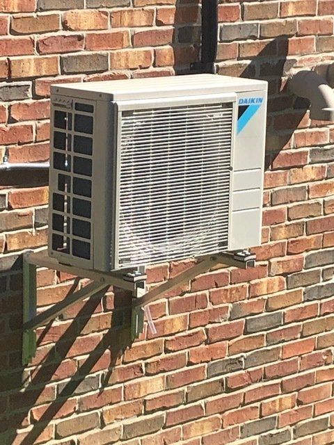 Wall-mounted air conditioner unit on a brick exterior wall in sunlight.