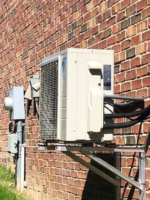 Outdoor air conditioner unit mounted on a brick wall with electrical boxes and cables.