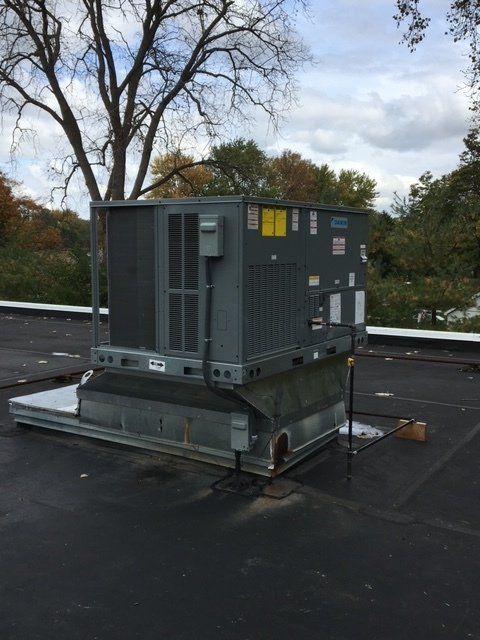 Technician kneeling beside a brick house, inspecting an outdoor HVAC unit with tools nearby.