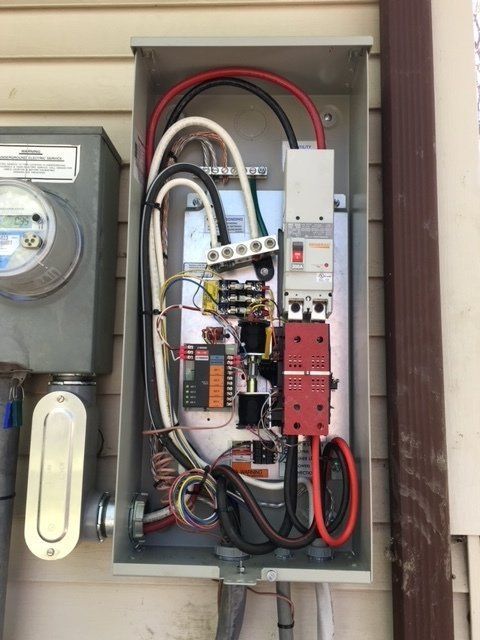 Open electrical service panel with exposed wiring and breakers mounted outside a house.
