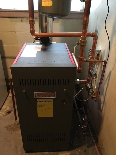 Gas furnace with copper pipes and black venting in a utility room.