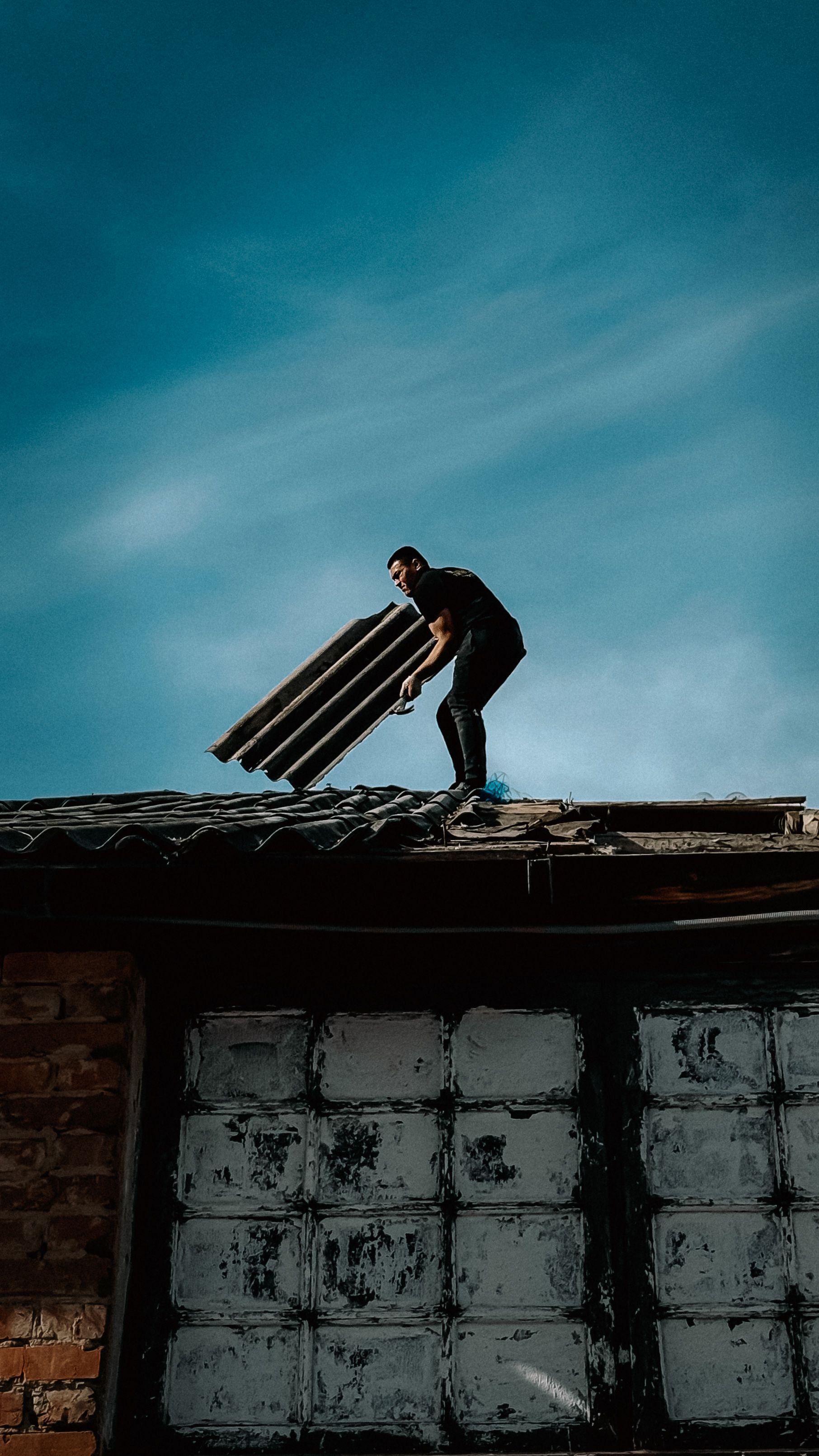 Worker on a rooftop carrying planks against a blue sky