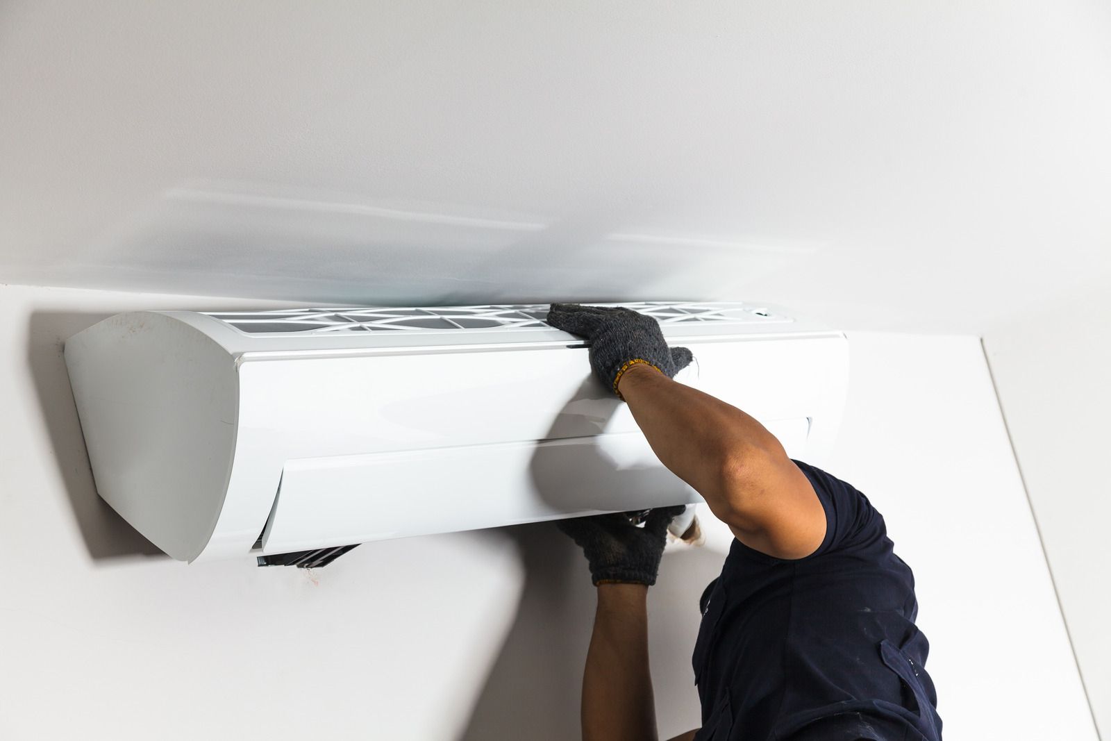Technician cleaning a wall-mounted air conditioner with a cloth on a white wall