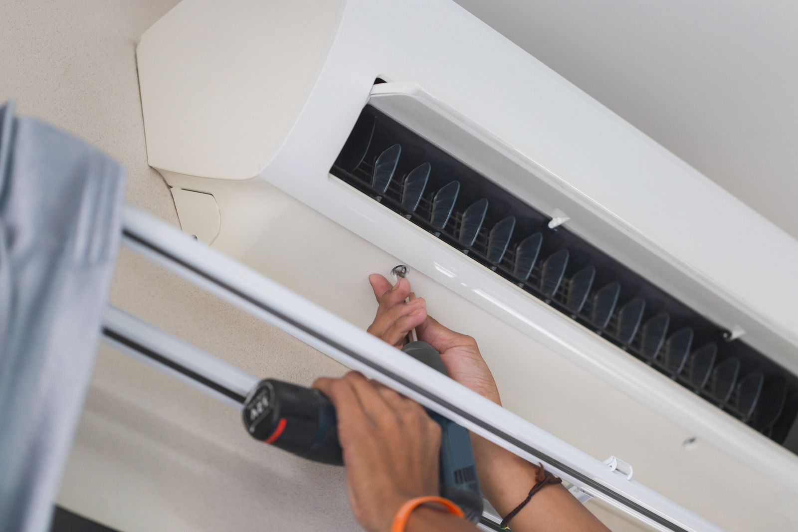 Person using a tool to repair a white wall-mounted air conditioner indoors