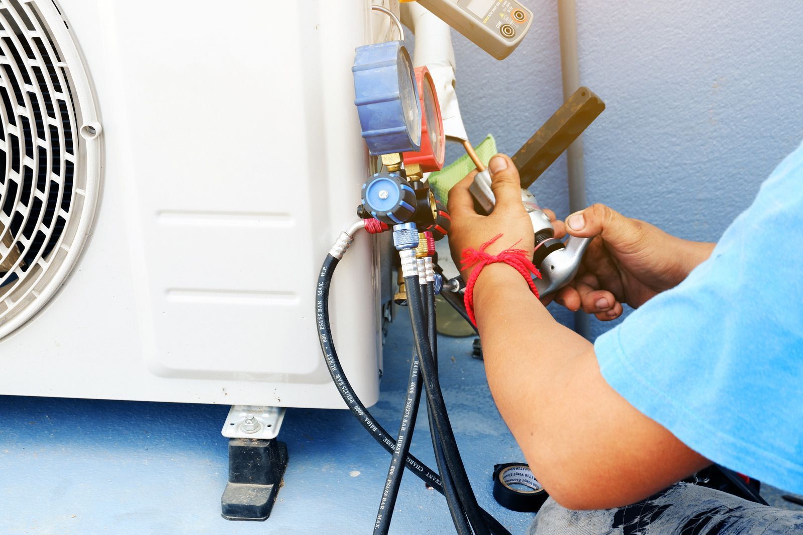 Technician connecting HVAC gauges to an outdoor air conditioner unit with hoses and tools