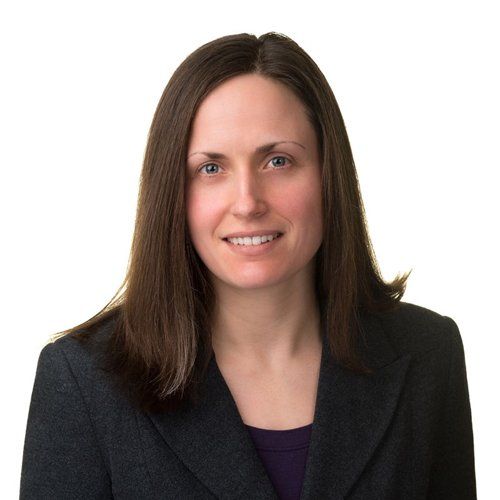 A woman wearing a black jacket and purple shirt smiles for the camera