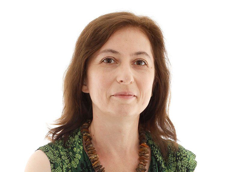 A woman wearing a green shirt and a necklace is looking at the camera.
