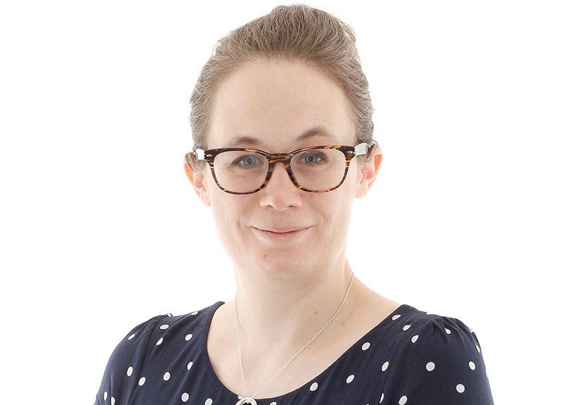 A woman wearing glasses and a polka dot shirt is smiling for the camera.