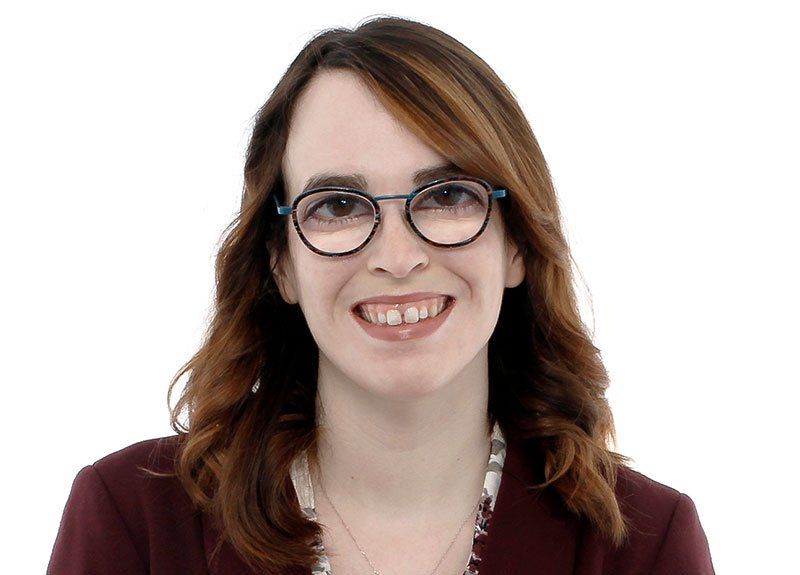 a woman wearing glasses and a maroon jacket smiles for the camera