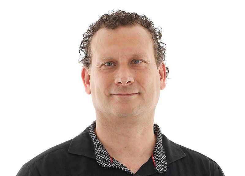 A man with curly hair is wearing a black shirt and smiling.