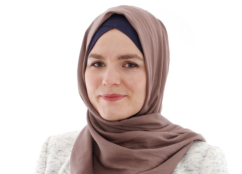 A woman wearing a hijab and a white jacket is smiling for the camera.
