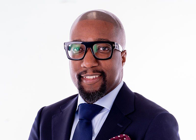 A man in a suit and tie with glasses and a beard is smiling.
